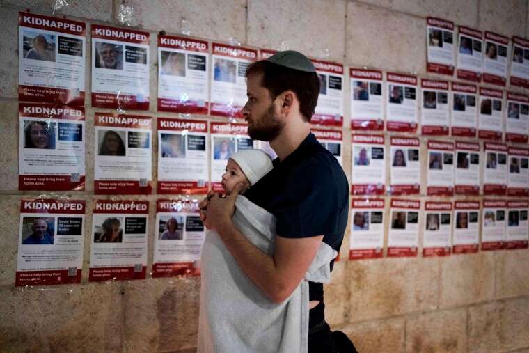 A man holds his baby as he looks at posters of the men, women and children held hostage by Hamas in the Gaza Strip during a vigil in Jerusalem on Nov. 5, 2023.