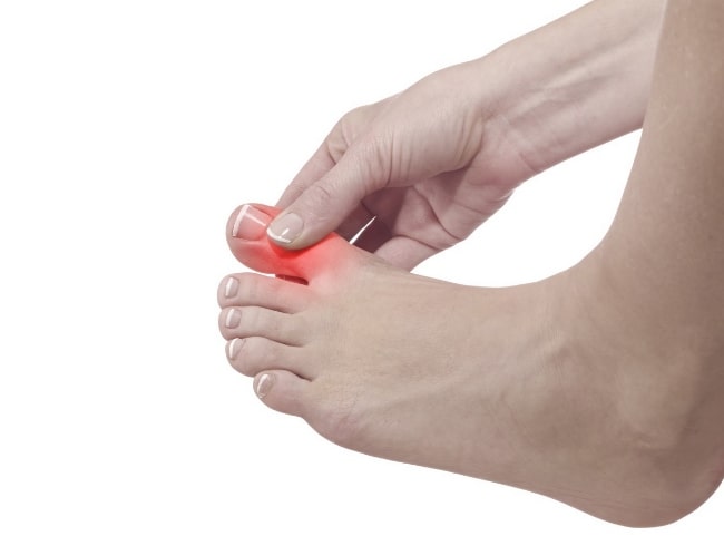 A person holding their painful big toe that is highlighted in red