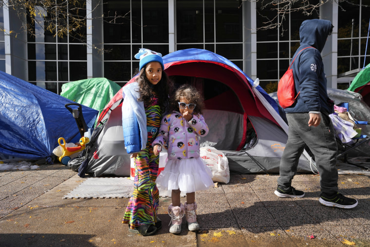 Migrant sisters Arantza, left, and Antonella pose wearing their Halloween costumes next to a small migrant tent community, Wednesday, Nov. 1, 2023, near a Northside police station in Chicago.
