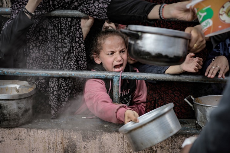 Palestinian children wait in line to receive food prepared by volunteers for Palestinian families displaced to Southern Gaza due to Israeli attacks, between rubbles of destroyed buildings in Rafah, Gaza on Feb. 10, 2024.