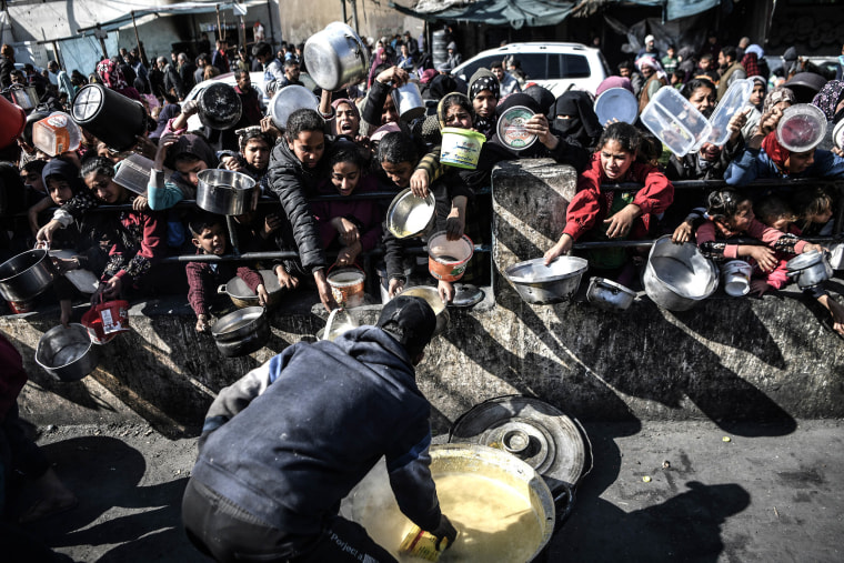 Palestinian people reach out for food with empty containers as food is distributed by charitable organizations while Israeli attacks continue in Rafah City of Gaza on Jan. 25, 2024.